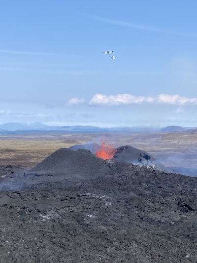 Silberne Flugzeuge fliegen über einen Vulkan, der Magma spuckt.