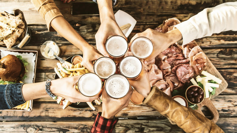 People clinking beer glasses over platters of food