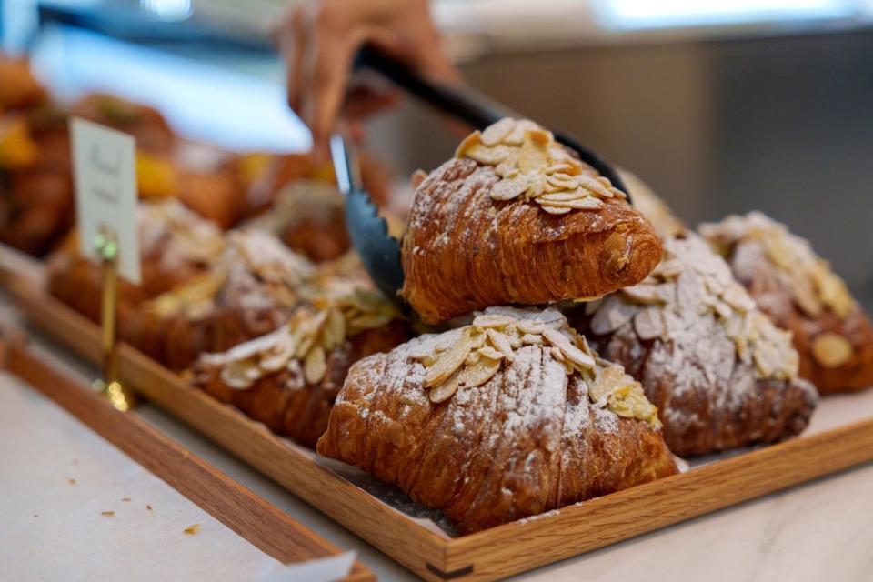Person using tongs to pick up an almond croissant from a bakery
