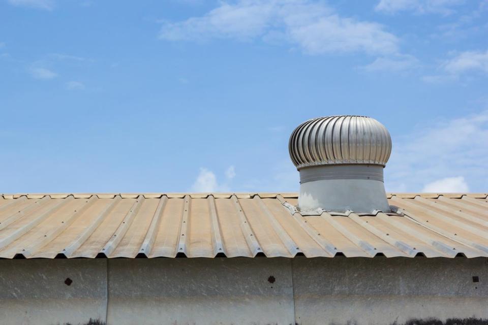 A close up of an attic fan on a tin roof against a bright blue sky. 