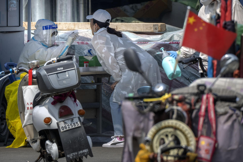 A worker wearing a protective suit swabs a woman's throat for a coronavirus test at a testing site near a building that was locked down after being linked to newly discovered COVID-19 cases in the Chaoyang district in Beijing, Friday, June 10, 2022. (AP Photo/Mark Schiefelbein)