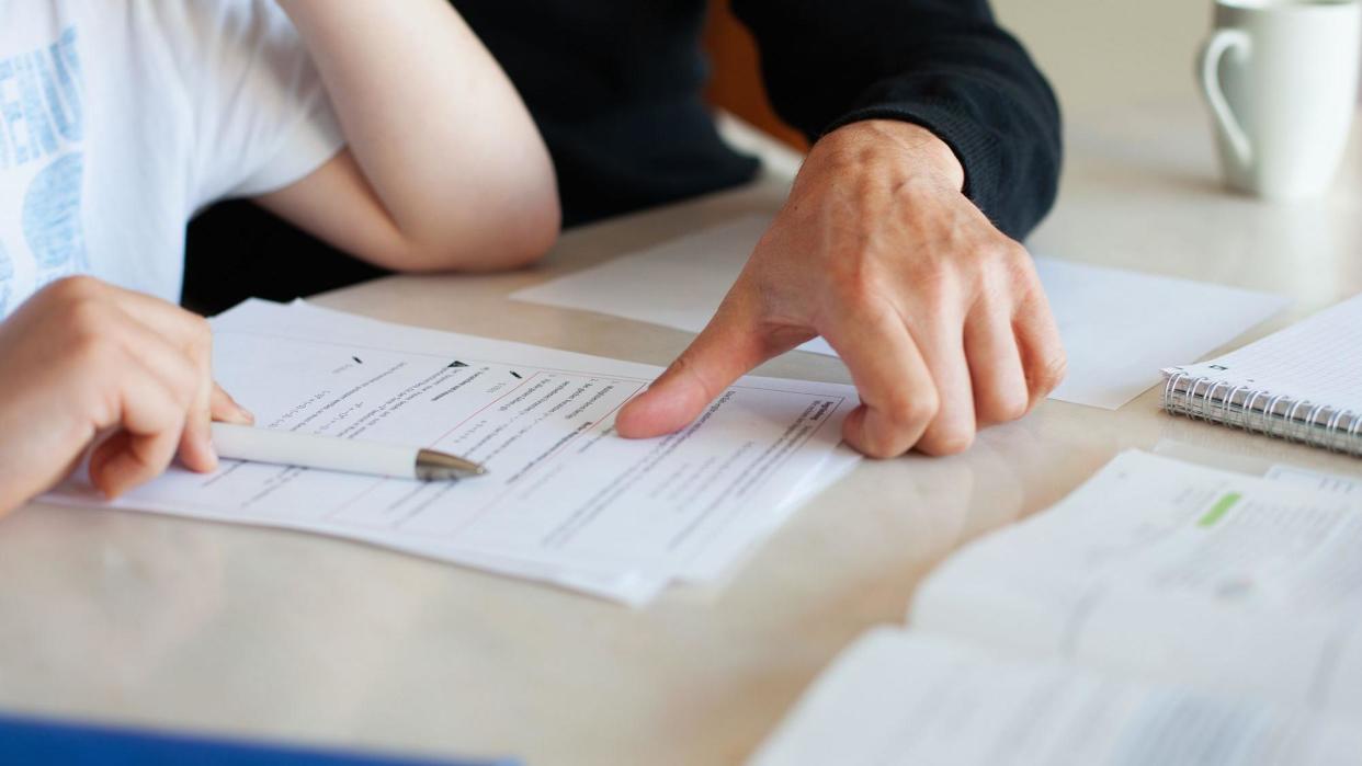 A close up of the hands of an adult an child looking at documents on a desk