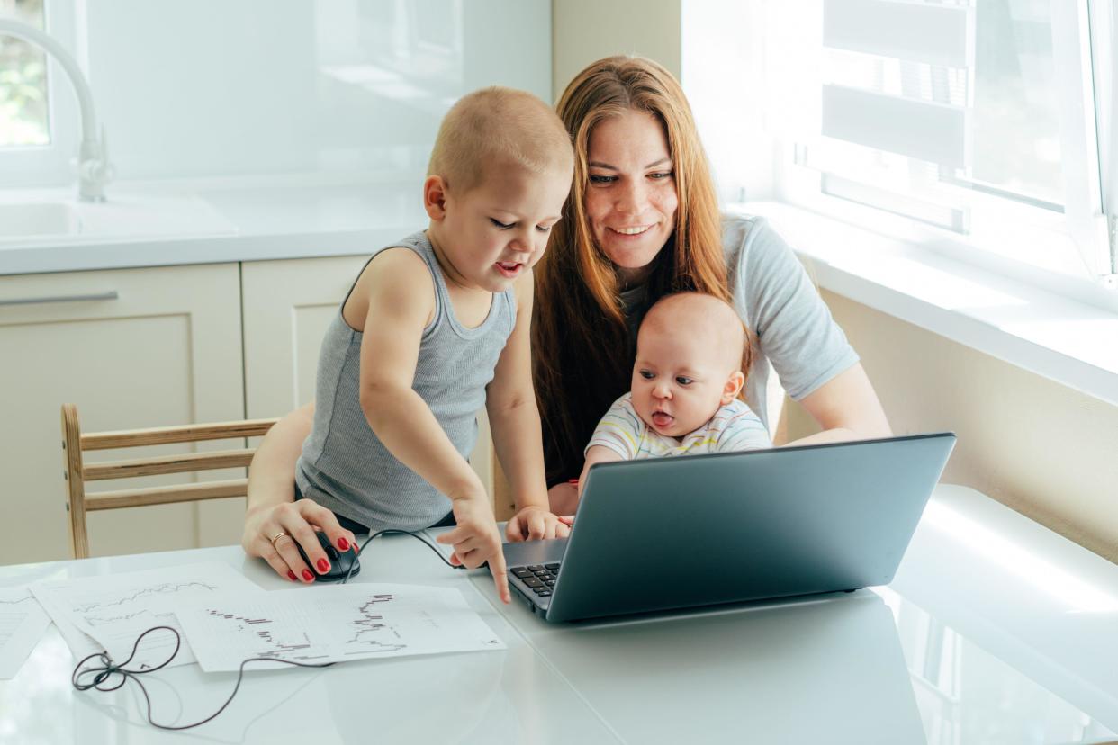 Young attractive mother with two children study online on a laptop in the kitchen at home.