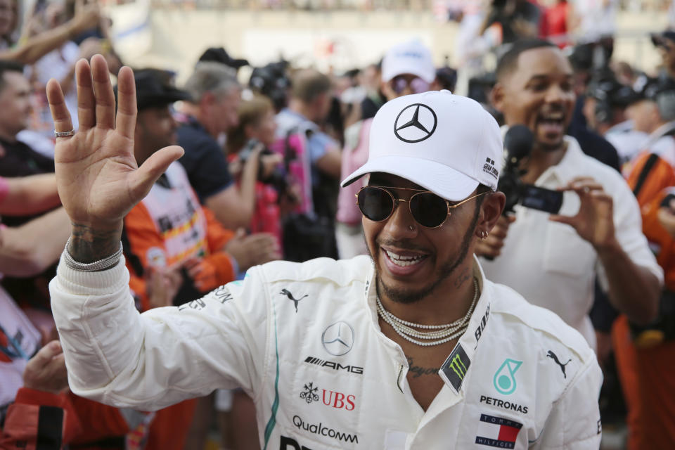 FILE - In this Sunday, Nov. 25, 2018 file photo, Mercedes driver Lewis Hamilton of Britain cheers with marshals, followed by US actor Will Smith, prior to the start of the Emirates Formula One Grand Prix at the Yas Marina racetrack in Abu Dhabi, United Arab Emirates. Even at the age of 34 and with five world titles, defending Formula One champion Lewis Hamilton is showing no sign of waning motivation. And it is that drive he will take into the new season as he bids to become only the second driver to win more than five world championships _ behind only seven-time winner Michael Schumacher. (AP Photo/Kamran Jebreili, file)