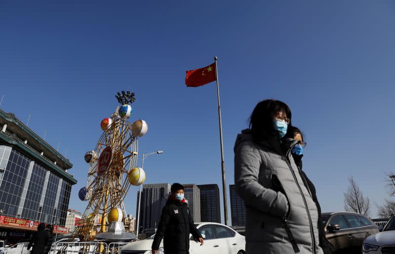 People wearing face masks walk past a Chinese flag, following new cases of the coronavirus disease (COVID-19) in the country, in Beijing