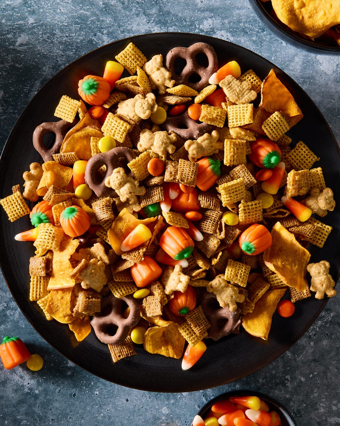 a bowl of halloween themed chex mix with chex cereal, chocolate pretzels, reese's pieces, candy corn, and sweet potato chips