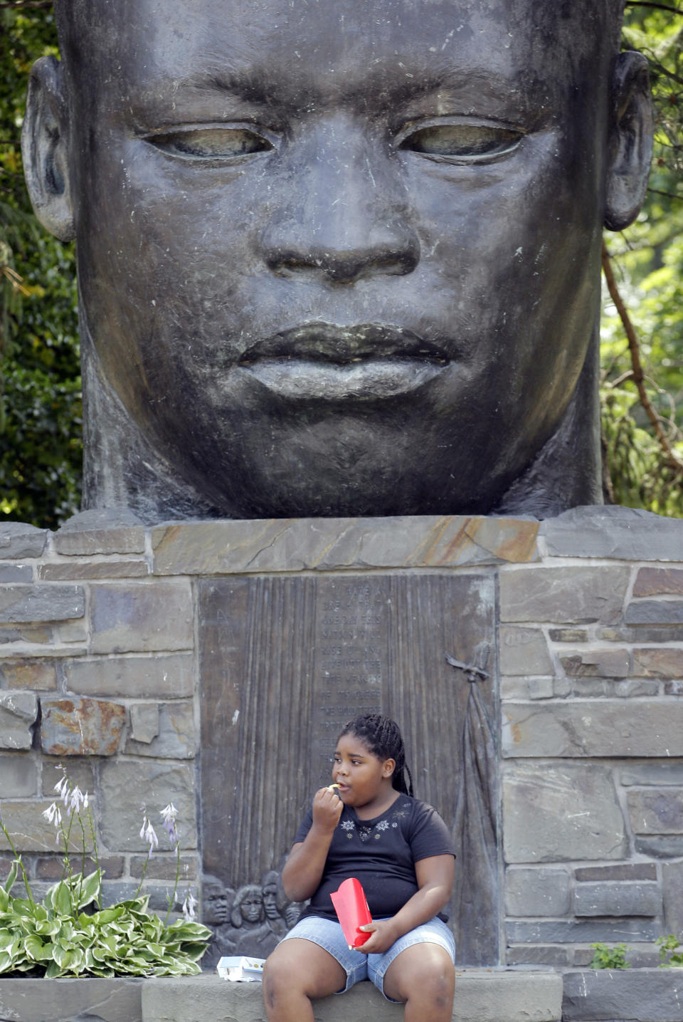 FILE - In this July 13, 2012 file photo, Tonae Johnson eats her lunch in the park in front of a Martin Luther King Jr. statue during the warm summer weather in Buffalo, N.Y. A community activist says he has gathered more than 6,000 signatures to replace the sculpture of the civil rights leader. Samuel Herbert says his goal is to get 10,000 signatures and a new statue by 2020. He says the 8-foot bust of King that sits in a namesake park in Buffalo doesn't look like the civil rights leader. (AP Photo/David Duprey, File)