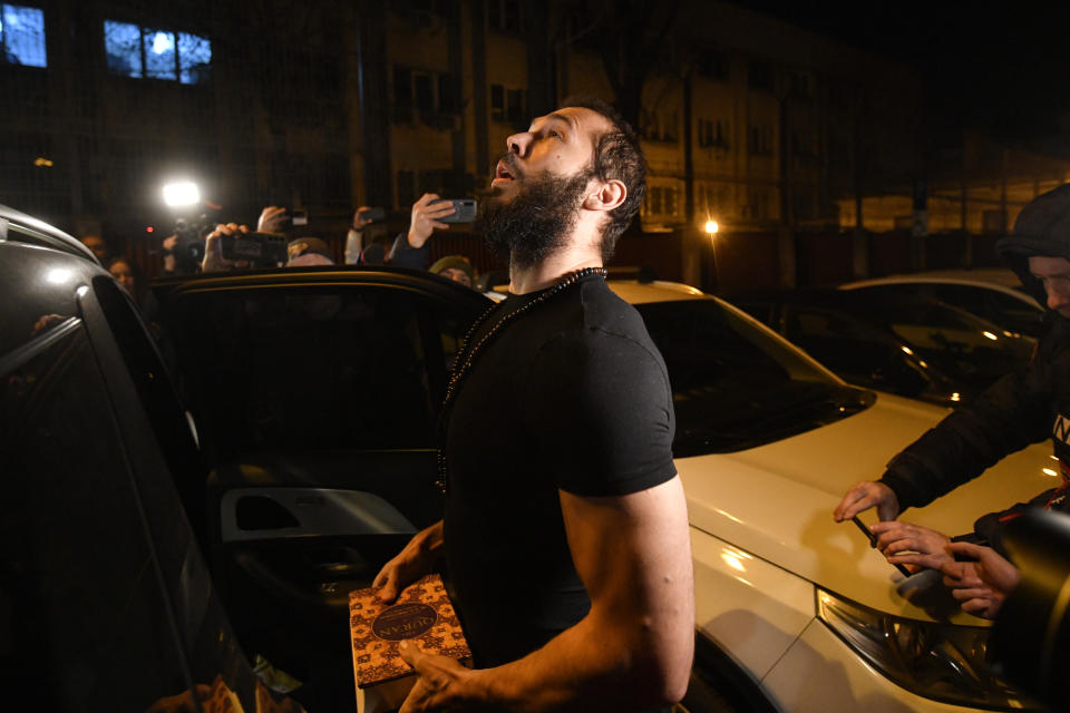 Andrew Tate looks up holding the Quran after leaving a police detention facility in Bucharest, Romania, on Friday March 31, 2023. An official on Friday said Tate, the divisive internet personality who has spent months in a Romanian jail on suspicion of organized crime and human trafficking, has won an appeal to replace his detention with house arrest. (AP Photo/Alexandru Dobre)