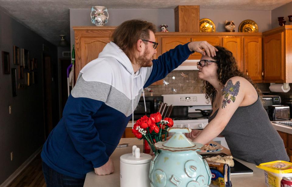 Charles Austin, 21, helps move the hair off the face of Amedy Dewey, 24, as she makes breakfast early in the morning inside her home in Scottville on Thursday, Jan. 25, 2024.