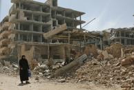 A Syrian woman walks past damaged buildings after a ceasefire came into effect in Zamalka, one of the few remaining rebel-held pockets in Eastern Ghouta, on the outskirts of the Syrian capital Damascus, on March 23, 2018 ahead of an evacuation deal