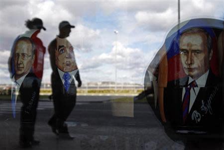 Police are reflected in the window of a shop displaying traditional nesting dolls with images of Russian President Vladimir Putin (R), Prime Minister Dmitry Medvedev (C) and French President Francois Hollande at the sea port in St. Petersburg September 3, 2013. REUTERS/Alexander Demianchuk