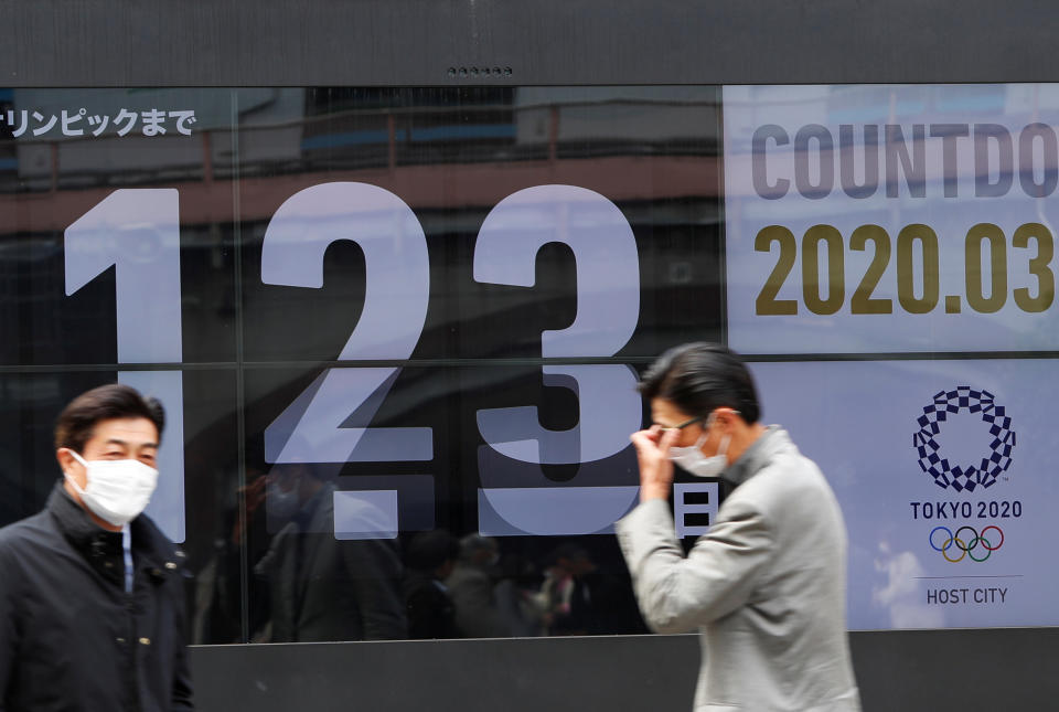 Passersby, wearing face masks due to the outbreak of the coronavirus disease (COVID-19), walk past a screen counting down the days to the Tokyo 2020 Olympic Games in Tokyo