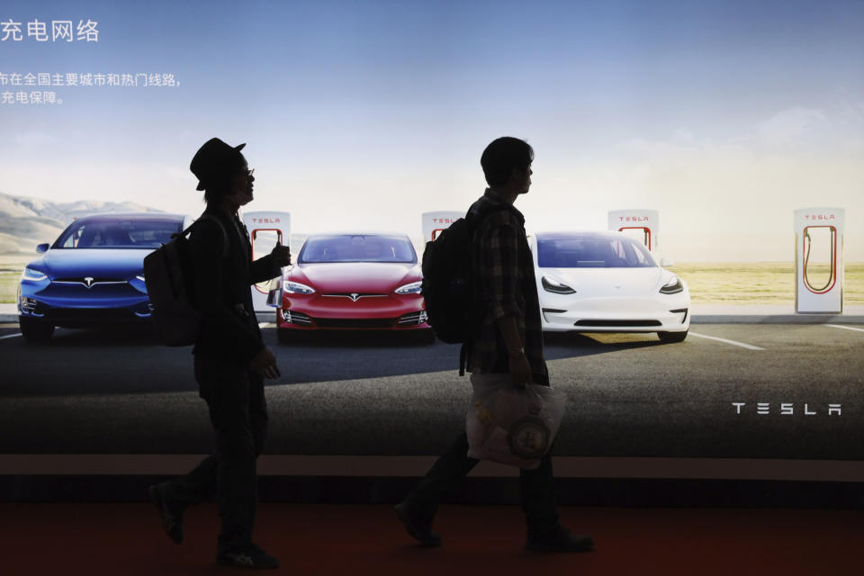 In this April 17, 2019, photo, attendees walks past advertisement for electric cars from Tesla at the Auto Shanghai 2019 show in Shanghai. China's electric car sales are stalling following the end of multibillion-dollar subsidies that made it the biggest market for the technology. Communist leaders want to make China a leader in electric cars but are shifting the burden to the industry by imposing mandatory sales quotas. (AP Photo/Ng Han Guan)