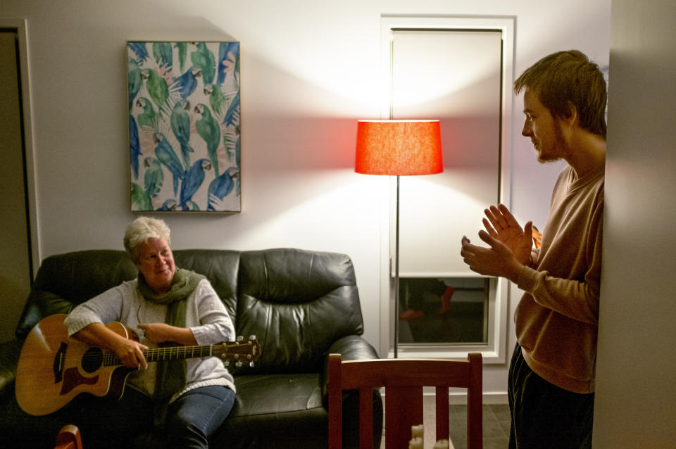 Sam Ware, right, claps as his mother, Deb Ware, finishes a song on the guitar at her home in Fountaindale, Central Coast, Australia, Friday, July 19, 2019. Sam was close to his mother, who had raised him on her own since he was a toddler, and who shared his fondness for music and the beach. Only three weeks earlier she said goodbye as doctors placed him into an induced coma, as a tsunami of opioids and other drugs roared through his battered body. (AP Photo/David Goldman)