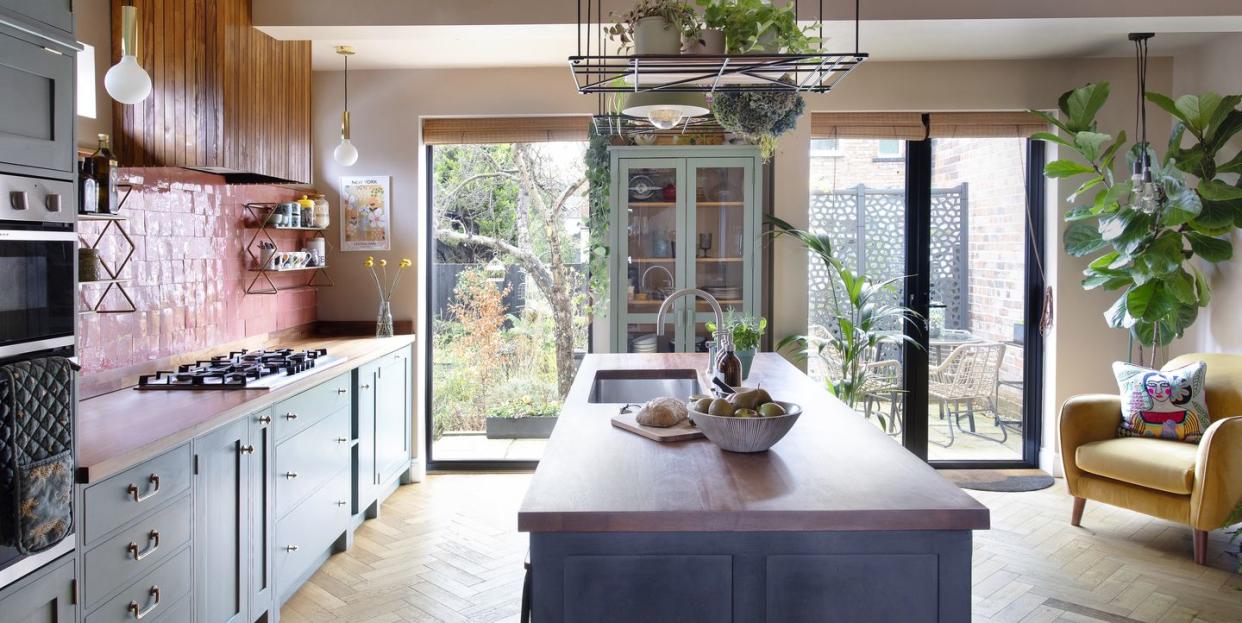 an open plan kitchen with pink zellige tiling as a splashback and plenty of greenery