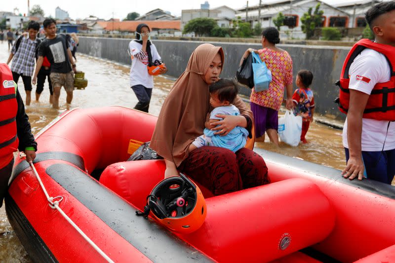 Woman holds a child as they are evacuated by an inflatable boat, at an area affected by floods after heavy rains in Jakarta
