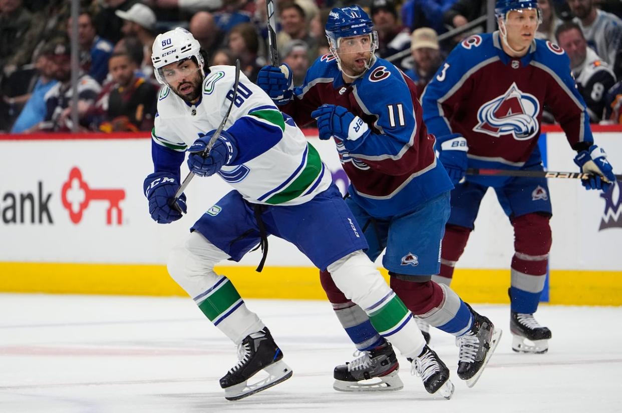 Vancouver Canucks left-winger Arshdeep Bains, left, pursues the puck with Colorado Avalanche center Andrew Cogliano at a game Tuesday. The Surrey-born hockey star made his NHL debut in Denver. (David Zalubowski/The Associated Press - image credit)