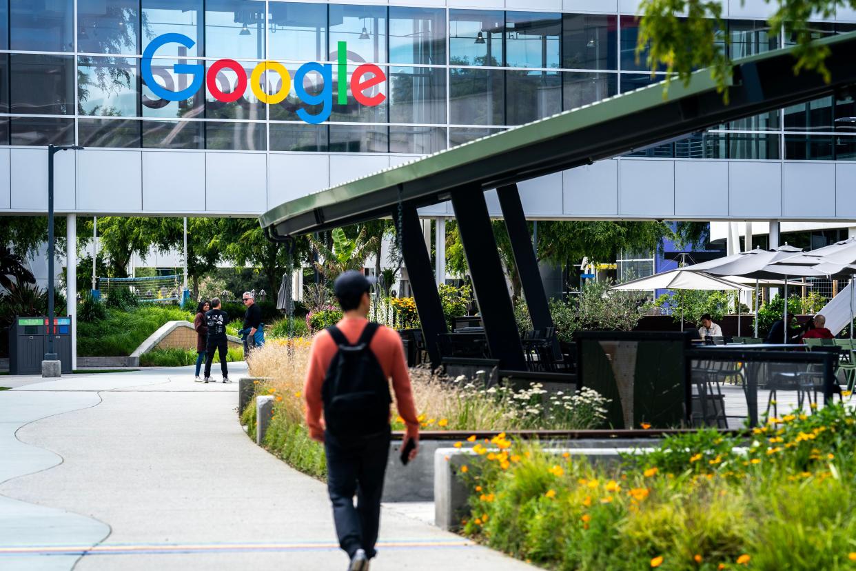 A man with a backpack walks up to a glass building with the Google logo on it