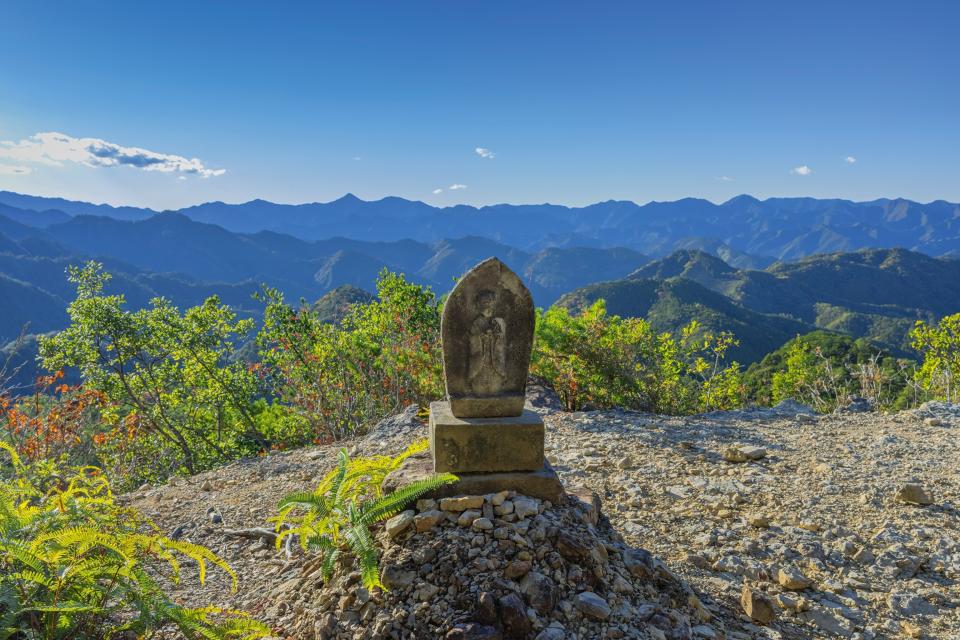 Stone statue stood among stones on top of a mountain viewpoint surrounded by blue skies