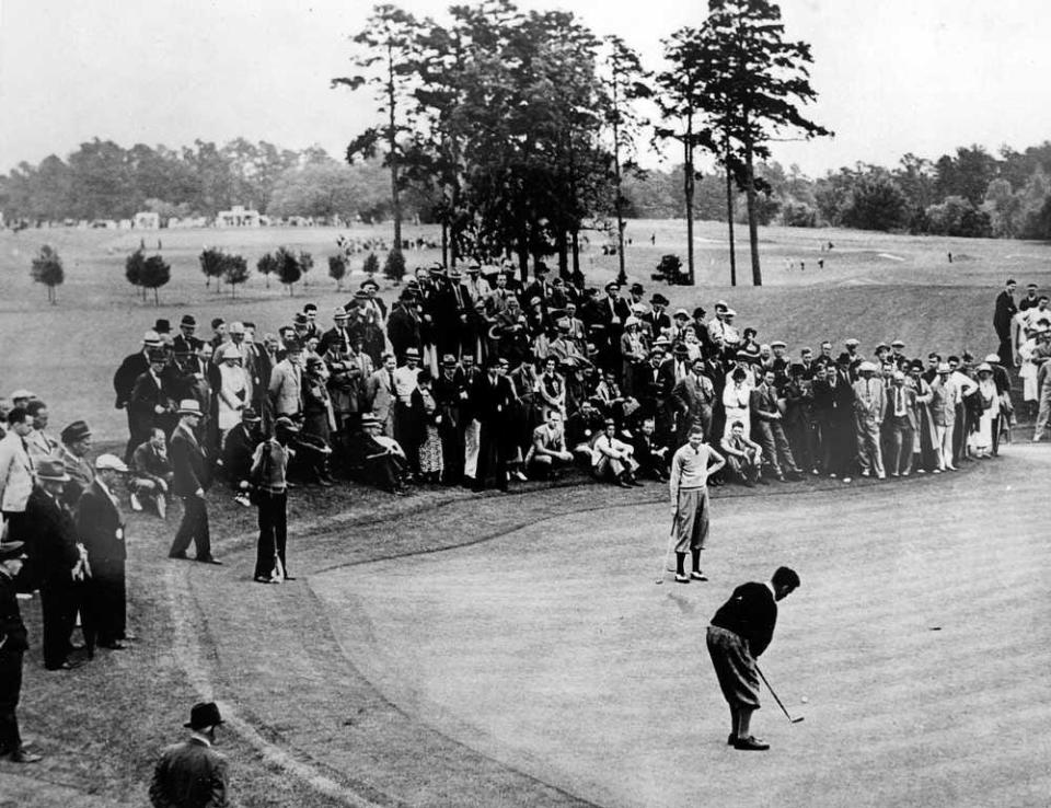 A photo shows the very first Masters Tournament in 1934. The inscription on the back reads "First Masters, 1934 - Bobby Jones putts as Horton Smith, the winner, looks on."