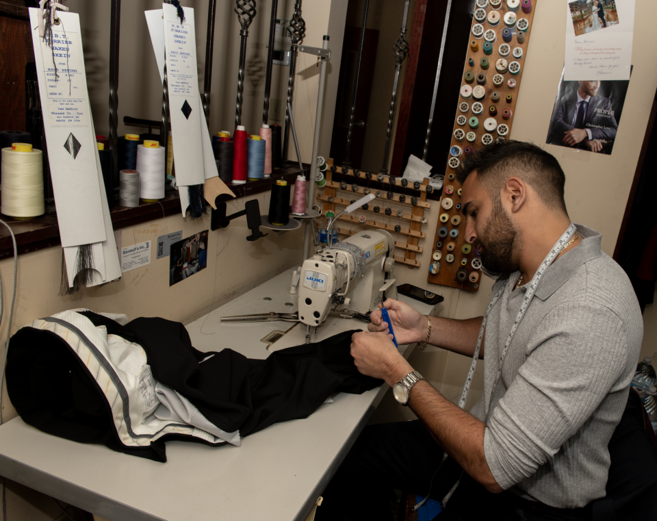 George Jabbour, the owner of Jabbour's Clothing & Tailoring in Stow, answers a phone call as he works on a pair of pants,