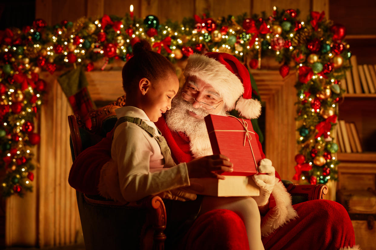 Side view portrait of cute African American girl opening Christmas present while sitting on Santas lap�