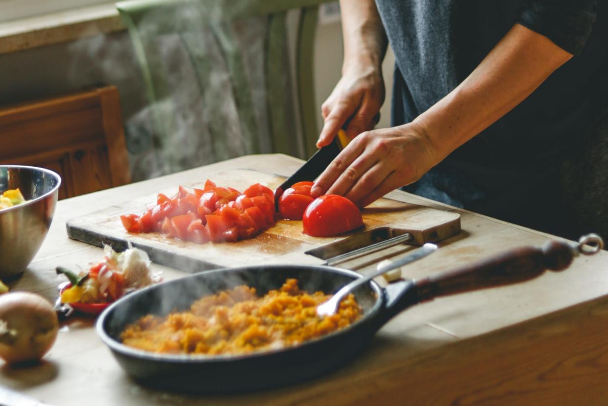 A woman chops tomatoes on a wooden table.