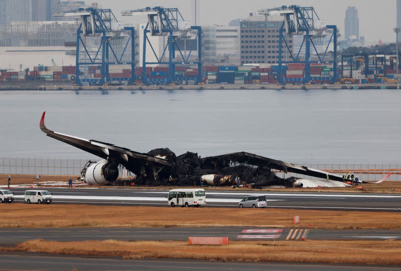 FILE PHOTO: Officials investigate a burnt Japan Airlines (JAL) Airbus A350 plane after a collision with a Japan Coast Guard aircraft at Haneda International Airport in Tokyo