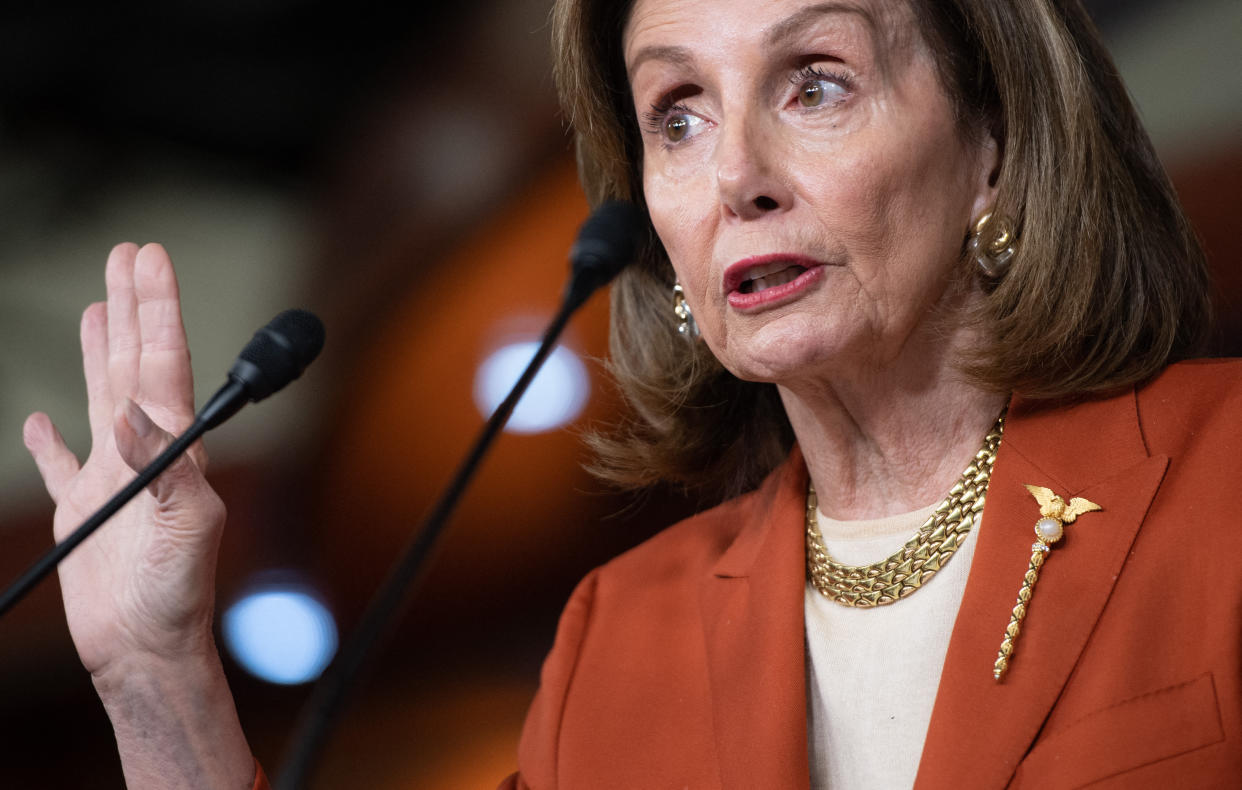 House Speaker Nancy Pelosi holds up her right hand as she speaks at a microphone during a press conference.