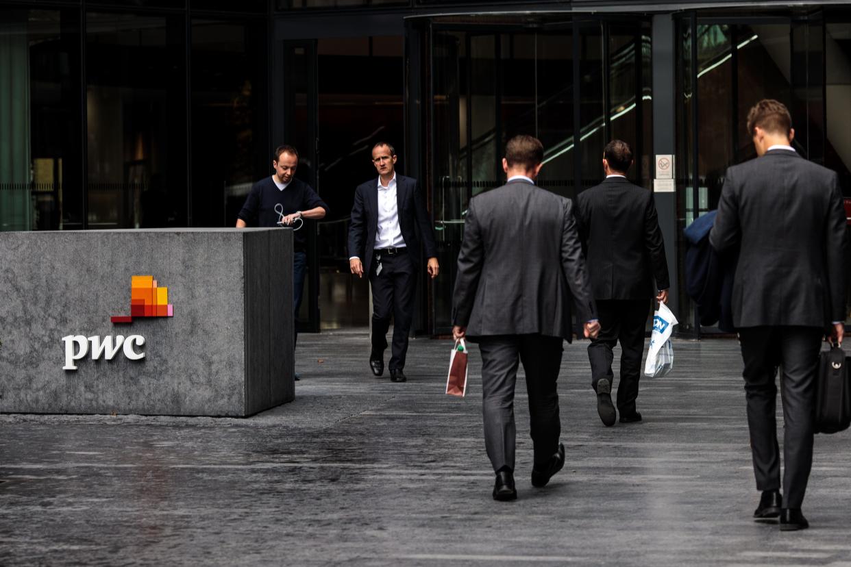 Workers walk by a sign for a PwC office