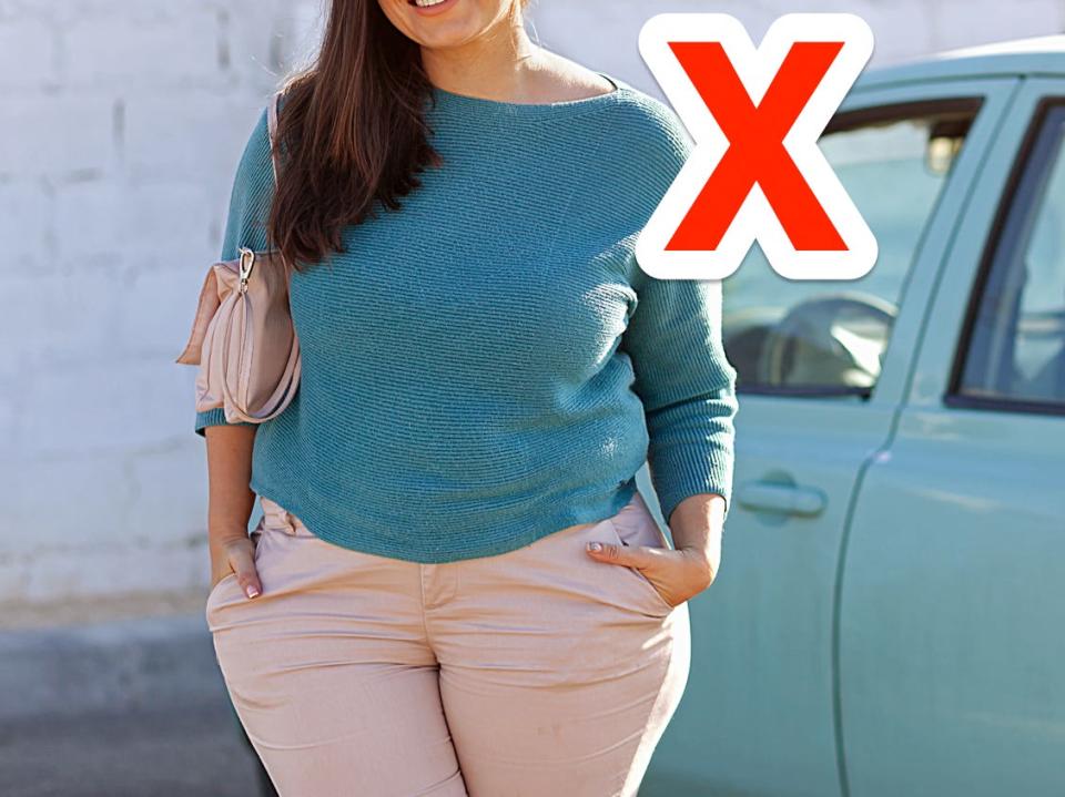 red x next to a person wearing a light blue sweater while standing in front of a blue car