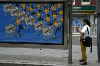 A resident waits at a bus-stop near an ad depicting shoppers in Beijing, Saturday, Aug. 13, 2022. China’s central bank trimmed a key interest rate Monday to shore up sagging economic growth at a politically sensitive time when President Xi Jinping is believed to be trying to extend his hold on power. (AP Photo/Ng Han Guan)