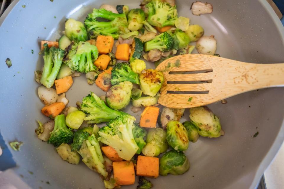 broccoli, carrots, sweet potatoes cooking in a pan with a spoon with slots pushing them around