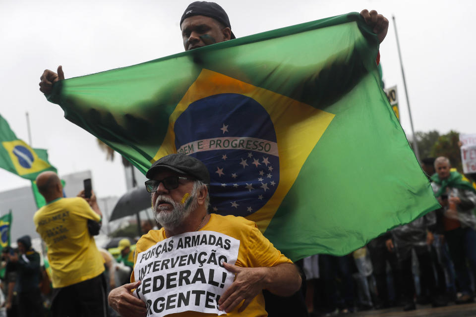 A supporter of President Jair Bolsonaro holds a sign with a message that reads in Portuguese: "Armed Forces, urgent federal intervention" during a protest against his defeat in the presidential runoff election, in Rio de Janeiro, Brazil, Wednesday, Nov. 2, 2022. Thousands of supporters called on the military Wednesday to keep the far-right leader in power, even as his administration signaled a willingness to hand over the reins to his rival Luiz Inacio Lula da Silva. (AP Photo/Bruna Prado)