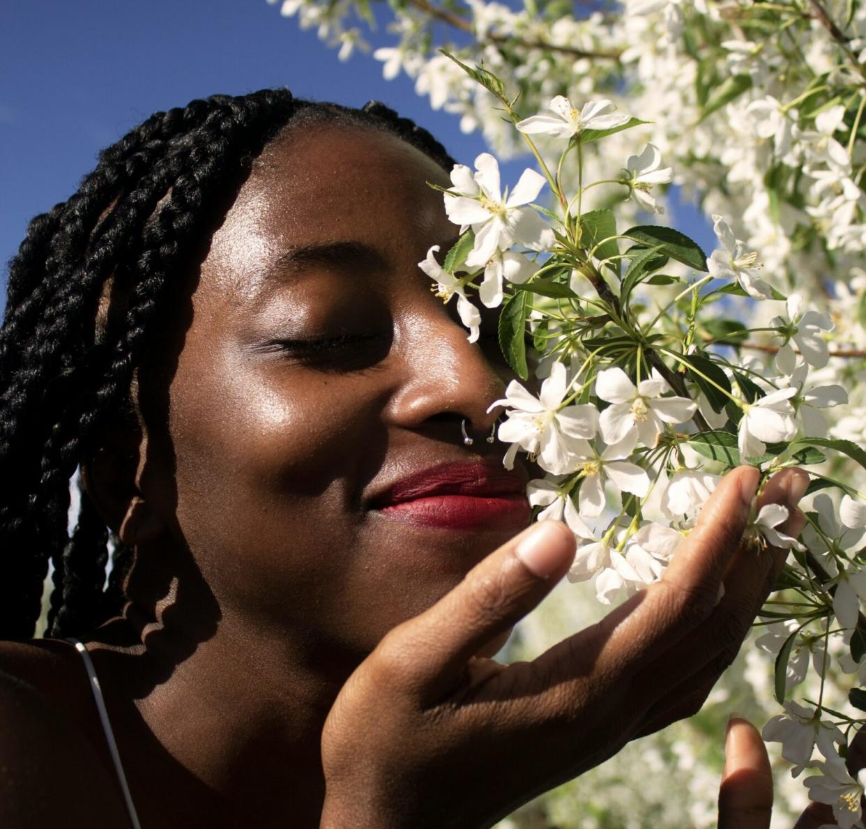 a Black woman smelling bloomed flowers on a bright sunny day