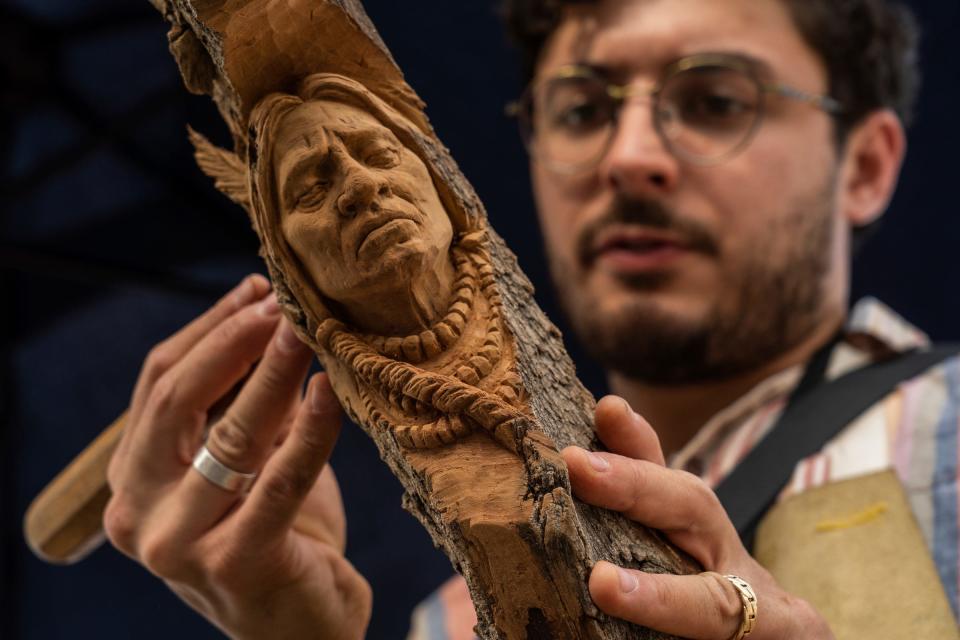 Alec Lacasse, of Oakland, carves a Native American figure in a piece of cottonwood at his boot while seeking some of his carvings during Arts, Beats & Eats in downtown Royal Oak on Sept. 2, 2022.