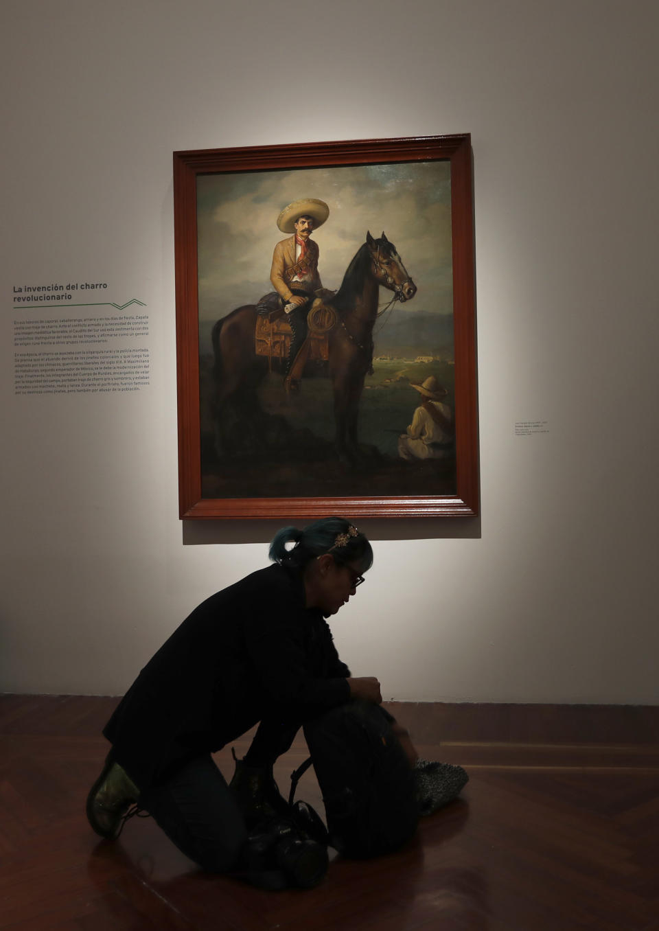 A journalist packs her backpack below a portrait of Mexican revolutionary hero Emiliano Zapata by Jose Atanasio Monroy, displayed during an exhibit remembering the one hundred anniversary of the death of Zapata, at the Bellas Artes Palace museum in Mexico City, Tuesday, Nov. 26, 2019. The exhibit features 140 art pieces and objects that belonged to Zapata. (AP Photo/Marco Ugarte)