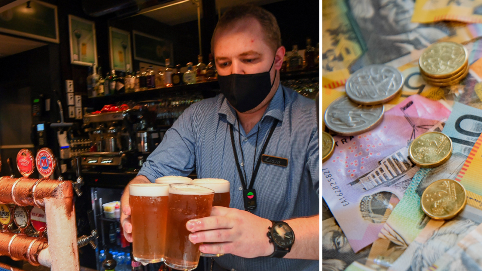 A man hands over four beers from behind the bar of a pub while wearing a mask and Australian currency with a mixture of notes and coins.