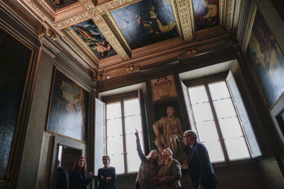 People look at the original site where the "Allegory of Inclination", top left, a 1616 work by Artemisia Gentileschi, now replaced by a photographic reproduction, before it was removed to undergo restoration, in the Casa Buonarroti Museum, in Florence, Italy, Wednesday, Nov. 9, 2022. Restorers have begun a six-month project on the "Allegory of Inclination" using modern techniques including x-rays and UV infrared research to go beneath the veils painted over the original to cover nudities and discover the work as Gentileschi painted it. (AP Photo/Andrew Medichini)