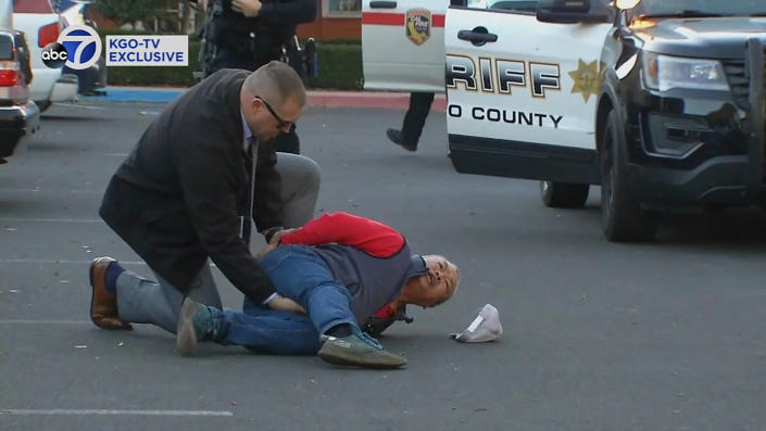 A suspect, on the ground, has his hands held behind his back by law enforcement. 