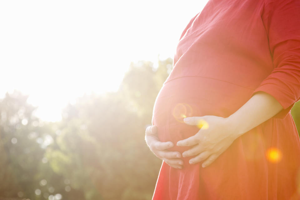 woman in red dress cradling her pregnancy bump