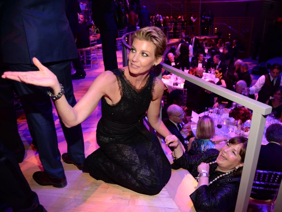 Faith Hill kneeling on a raised platform, holding the arm of Ina Garten, who is below her.