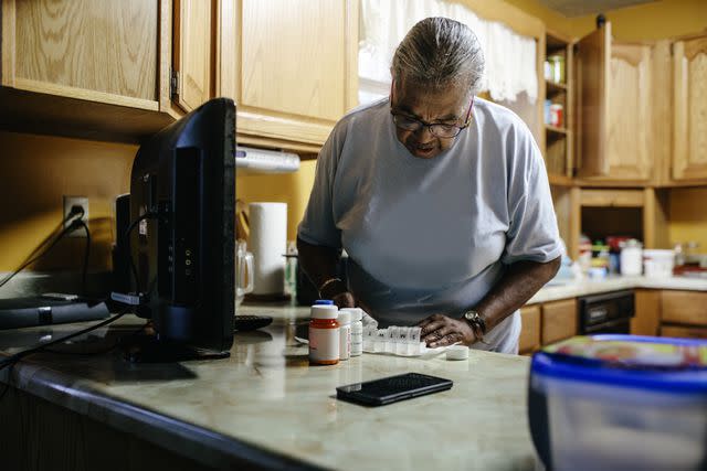 <p>Willie B. Thomas / Getty Images</p> Older black female standing in kitchen sorting her medication.