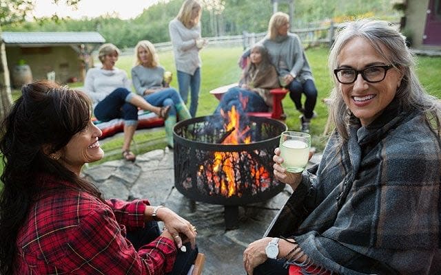 smiling woman with friends at fire backyard - Credit: alamy.com