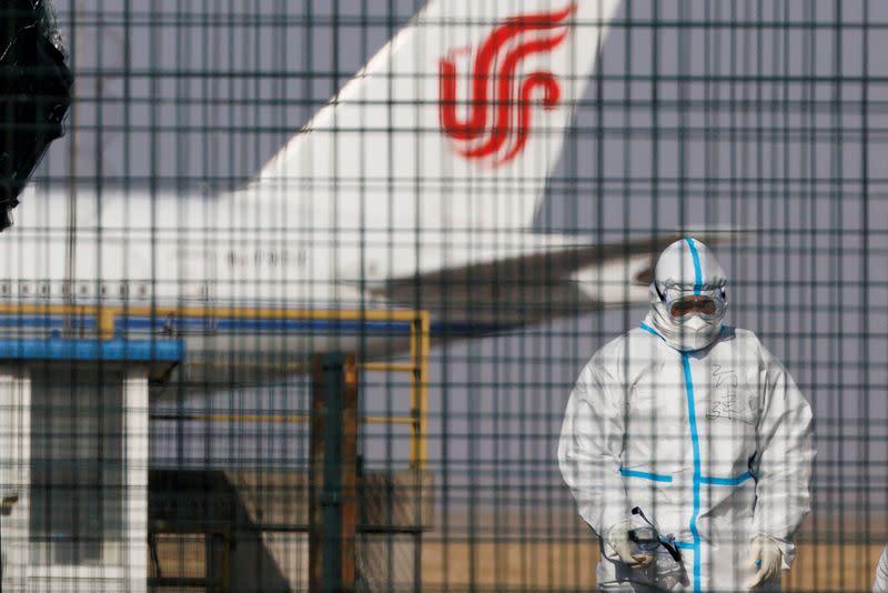 FILE PHOTO: A worker in a protective suit walks near a plane of Air China airlines at Beijing Capital International Airport as coronavirus disease (COVID-19) outbreaks continue in Beijing