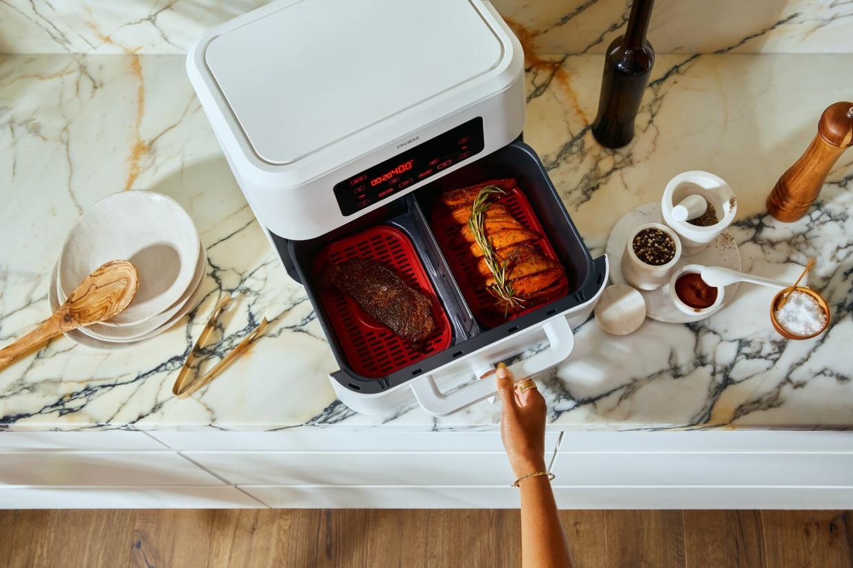 large white air fryer with a steak and potatoes in the two baskets on a large white kitchen counter