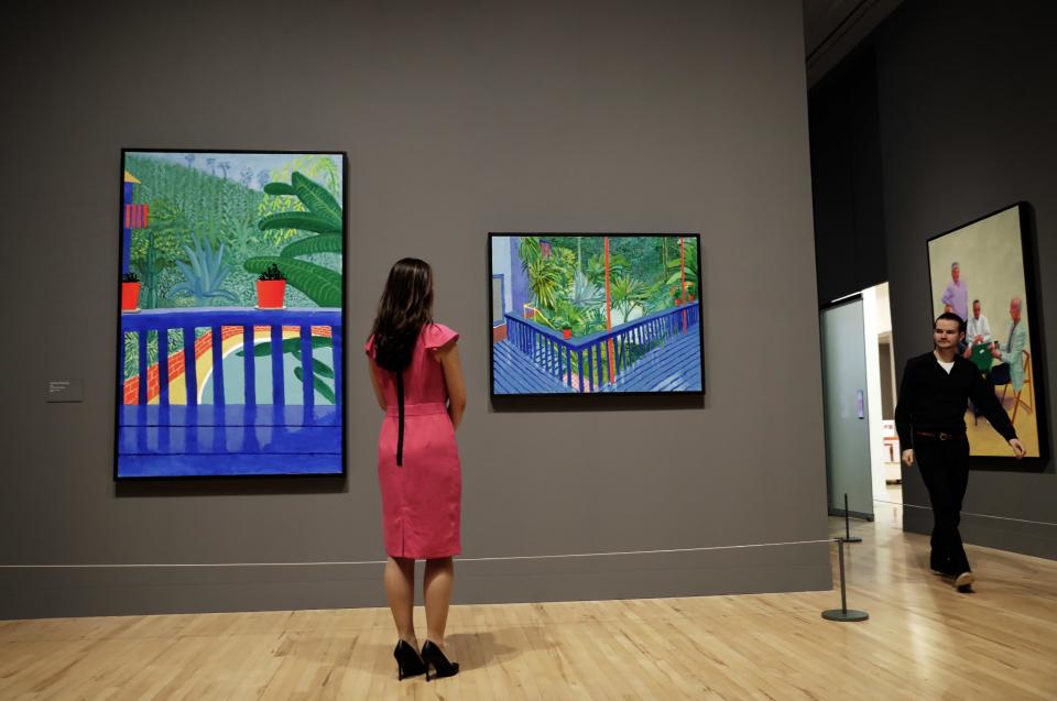 A Tate representative poses for photographs next to David Hockney's Los Angeles garden paintings "Two Pots on the Terrace", left, and "Garden #3" during a photocall to promote the largest-ever retrospective of his work at Tate Britain gallery in London, Monday, Feb. 6, 2017. The exhibition, which opens to the public from February 9 and runs until May 29, celebrates the 79-year-old's achievement in painting, drawing, photography and video. (AP Photo/Matt Dunham)