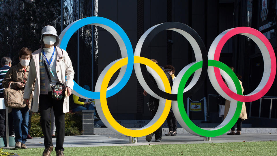 Women with surgical masks, pictured here walking next to the Olympic Rings.