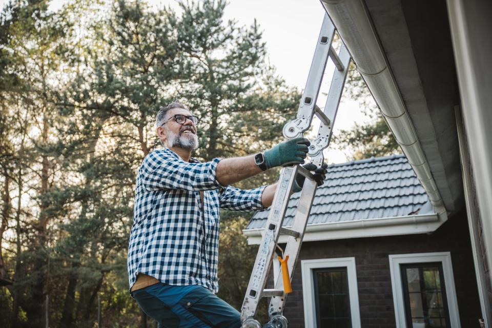 man cleaning leaves from guttering of house