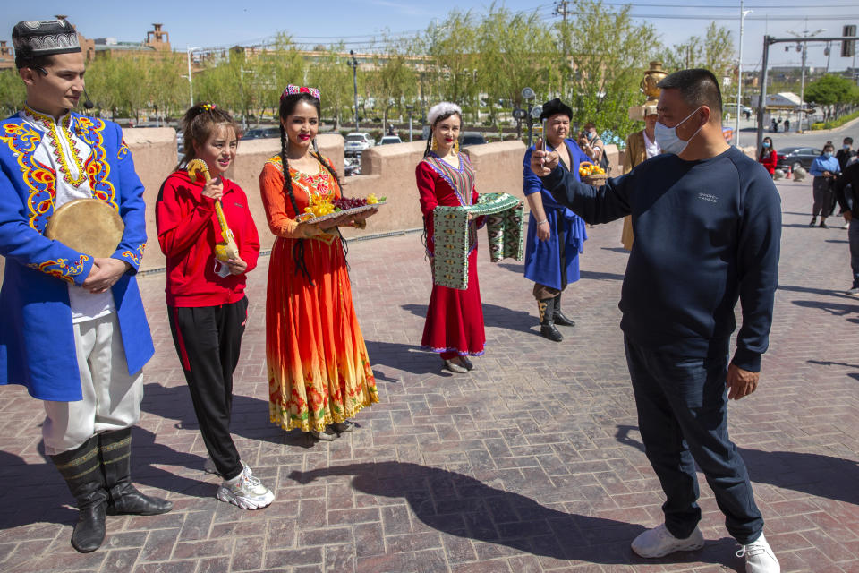 FILE - A tourist snaps pictures of Uyghur performers at the front gate of the remodeled city center of Kashgar in China's far west Xinjiang region, during the welcome ceremony of a state tour for foreign media on April 19, 2021. After a U.N. report concluding that China's crackdown in the far west Xinjiang region may constitute crimes against humanity, China used a well-worn tactic to deflect criticism: blame a Western conspiracy. (AP Photo/Mark Schiefelbein, File)